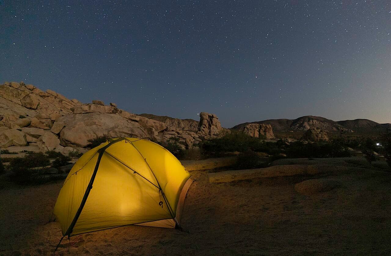 A glowing tent beneath a starry sky among rock formations at a campground.