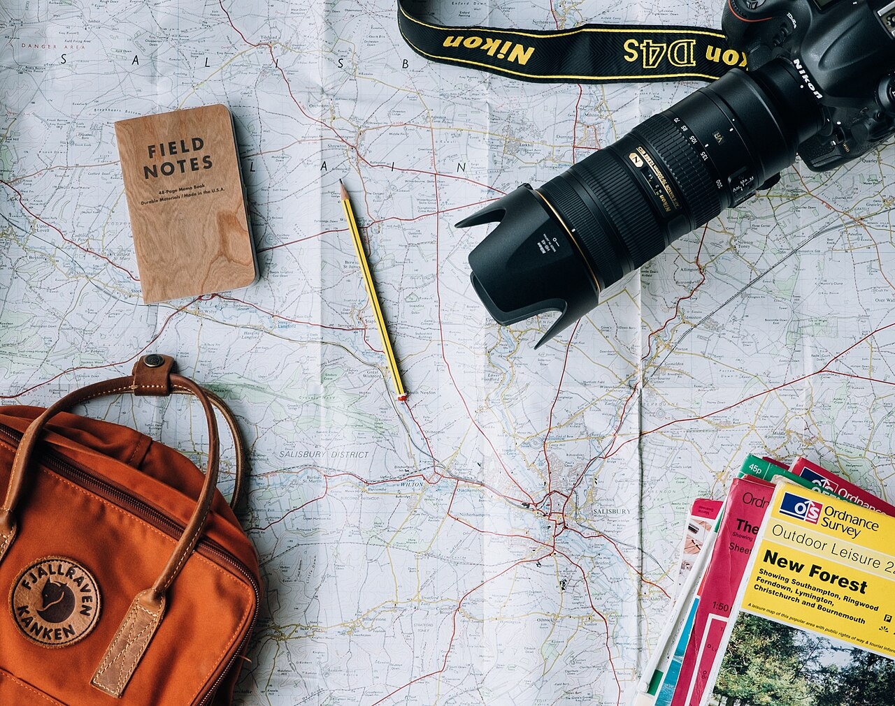 A camera, notebook, pencil and travel bag arranged on a map for trip planning.